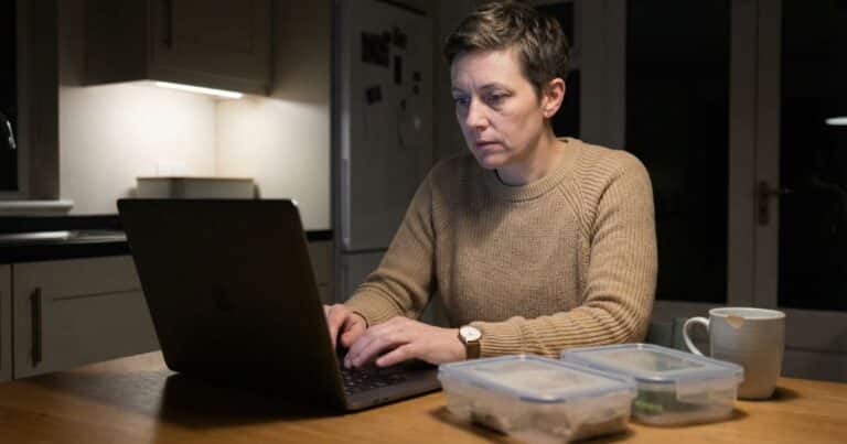 Humanize AI text: content creator staring at dull laptop draft at kitchen table beside empty meal prep containers