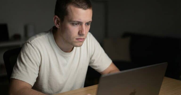 Young course creator looking at ChatGPT results on laptop at night, worried AI recommendations not including his course